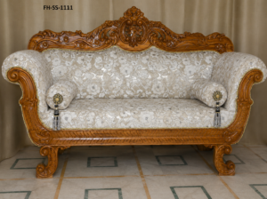 Luxurious handcrafted wooden sofa featuring intricate floral carvings, elegant cream floral upholstery, rolled arms, decorative bolster cushions, and a polished natural wood finish.