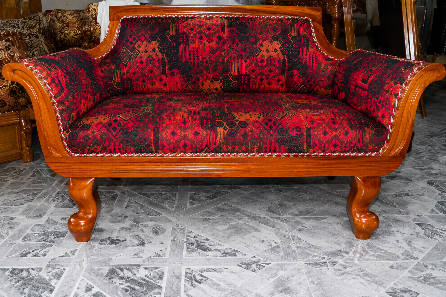Premium solid wood designer lounge sofa featuring a polished natural wood frame, curved armrests, and bold red geometric patterned upholstery for modern living spaces.