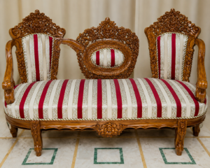 Elegant handcrafted royal chaise lounge sofa with intricate solid wood carvings, striped cream and burgundy upholstery, decorative center crest, and classic luxury design.