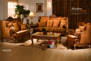 Elegant handcrafted wooden sofa set featuring intricate carvings, premium golden upholstery, matching armchairs, decorative cushions, and a classic wooden center table in a luxurious living room setting.