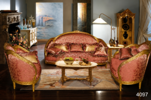 Elegant blush pink luxury sofa set with gold-finished carved wooden frame, premium patterned upholstery, decorative cushions, matching armchairs, and a marble-top coffee table in a sophisticated classic living room.